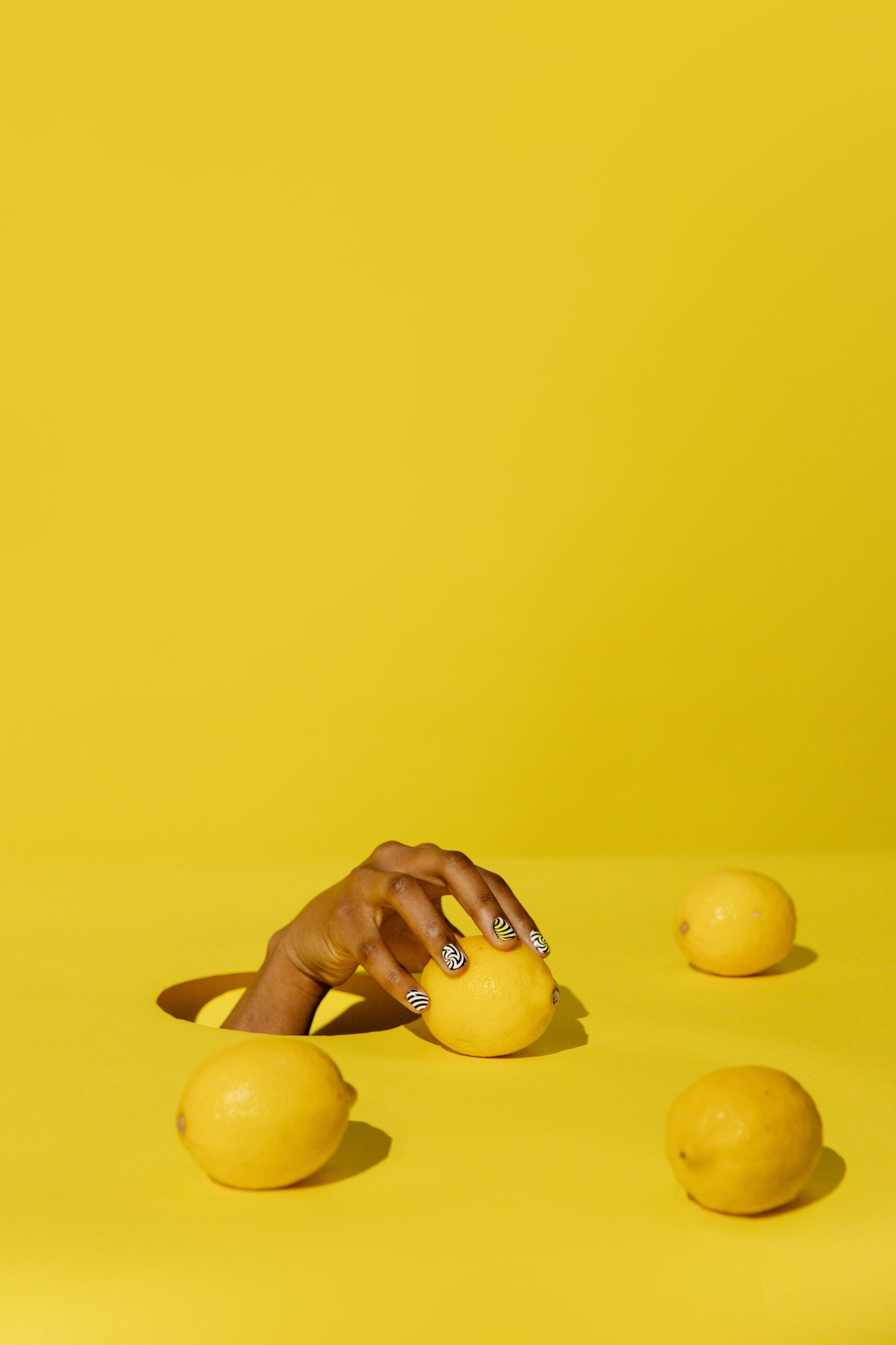 LEMONS LAYING ON A TABLE WITH A HAND COMING THROUGH A HOLE IN TABLE.